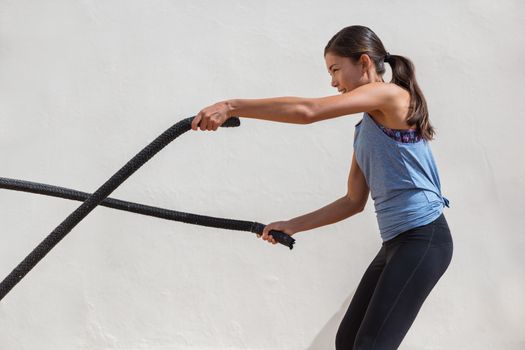 Fitness woman training battle ropes workout at gym. Girl working out arms and cardio using battling rope for cross fit exercises.