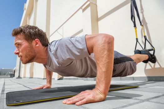 Fitness man doing pushups using suspension straps at fitness centre. Athlete doing bodyweight push-up exercises on floor outdoors.