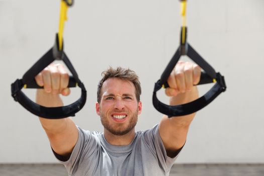 Suspension straps exercises man training arms workout at outdoor gym. Athlete holding suspended trx handles doing inclined pull-ups for back muscles.