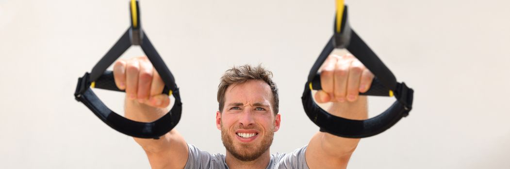 Fitness man trx banner suspension resistance straps training. Athlete holding handles doing inclined pull-ups for back and biceps muscles at gym. Panorama horizontal crop.