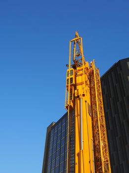 a folded yellow construction crane with gantry strapped to the side waiting to be deployed on an urban building site