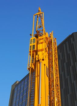 a folded yellow construction crane with gantry strapped to the side waiting to be deployed on an urban building site