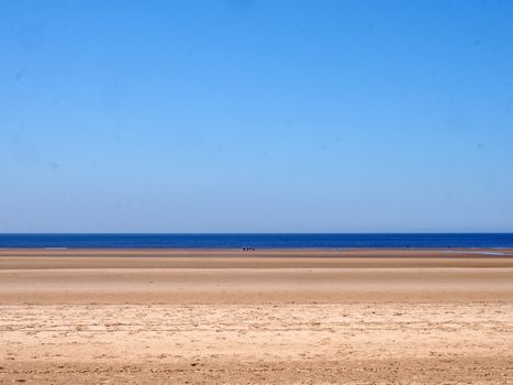 a long sandy beach with blue summer sky and blue sea with a group distant unidentifiable people near the water
