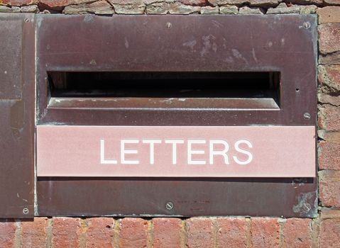 an old british postal mail box in a brick wall with rusted metal surround and the word letters on a faded red panel