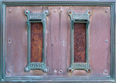 old british postal mail boxes with rusted letter slots and ornate green copper frames with the words postage stamps surrounded by an old stained metal frame