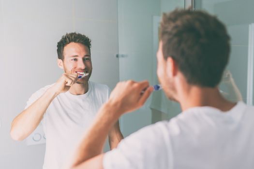 Brushing teeth man looking in mirror of home bathroom using toothbrush in morning routine for clean dental oral care.