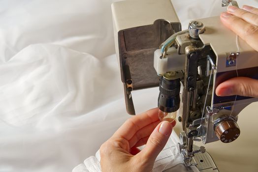 Woman's hands setting sewing machine. worker changing bulb in sewing machine