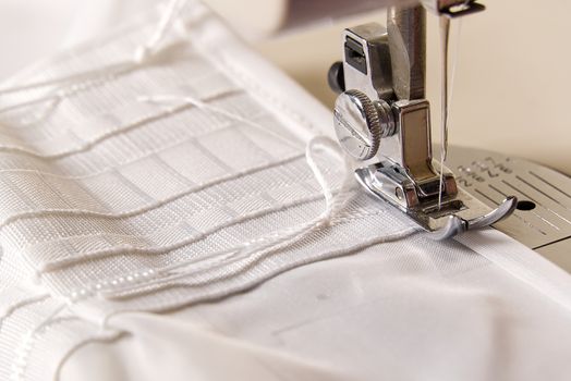 A worker works on a sewing machine. seamstress sews white curtains, close up view