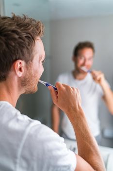 Man brushing teeth in the morning looking in bathroom mirror using toothbrush and toothpaste. Home lifestyle, dental hygiene care. Oral health.