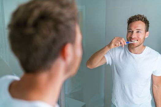 Brushing teeth man looking in mirror of home bathroom using toothbrush in morning routine for clean dental oral care.