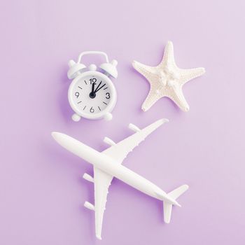 World Tourism Day, Top view flat lay of minimal toy model plane, airplane, starfish, alarm clock and compass, studio shot isolated on a purple background, accessory flight holiday concept