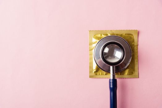 World sexual health or Aids day, Top view flat lay medical equipment, condom in pack and stethoscope, studio shot isolated on a pink background, Safe sex and reproductive health concept