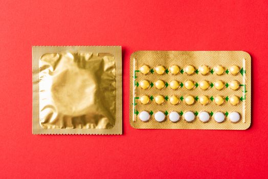 World sexual health or Aids day, condom on wrapper pack and contraceptive pills blister hormonal birth control pills, studio shot isolated on a red background, Safe sex and reproductive health concept