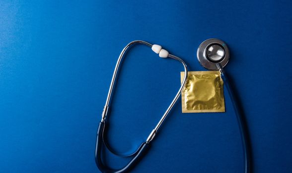 World sexual health or Aids day, Top view flat lay medical equipment, condom in pack and stethoscope, studio shot isolated on dark blue background, Safe sex and reproductive health concept