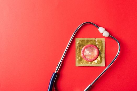 World sexual health or Aids day, Top view flat lay medical equipment, condom in pack and stethoscope, studio shot isolated on a red  background, Safe sex and reproductive health concept