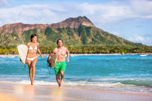 Happy surf people having fun surfing on Waikiki beach, Honolulu, Oahu, Hawaii. Asian woman, caucasian man multiracial couple running out of ocean splashing water. Summer vacations travel landscape.