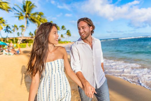 Beach couple happy holding hands on hawaiian holidays in Waiohai beach, Poipu in Kauai, Hawaii, USA. Newlyweds people in love on honeymoon. Asian woman, Caucasian man.