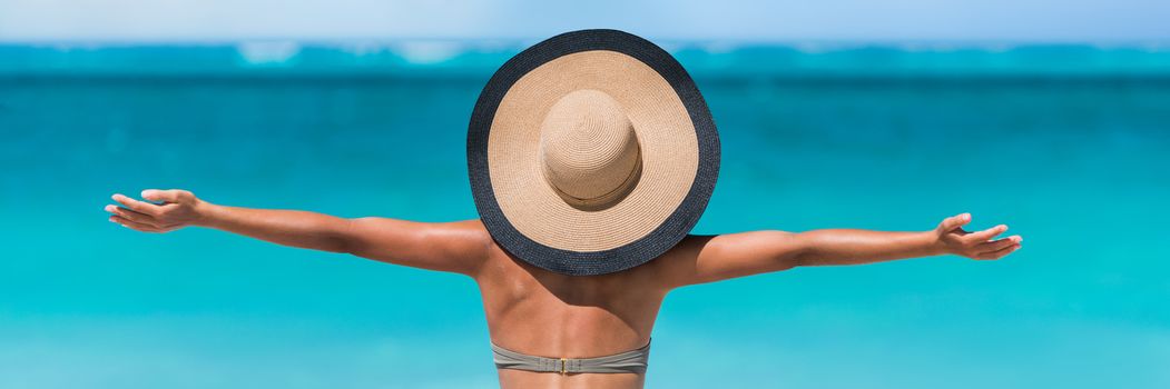 Beach vacation freedom summer travel holidays banner panorama. Woman in sun hat and bikini with open arms raised to the sky enjoying looking view of beach blue ocean.