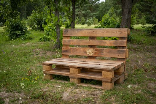 Outdoor furniture made from wood pallets surrounded by trees and greenery in summer sunshine