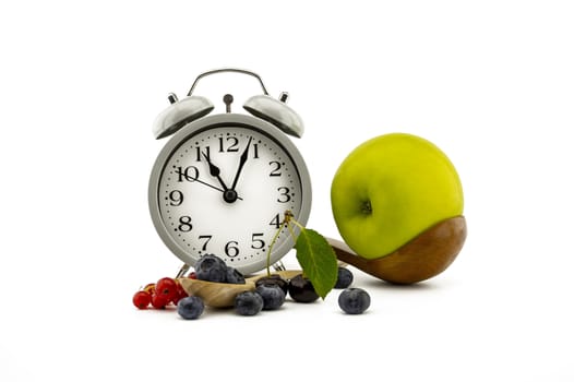 Culinary still life with old-fashioned alarm clock, wooden spoon, cherries, red currants, green apple and blueberries over white background
