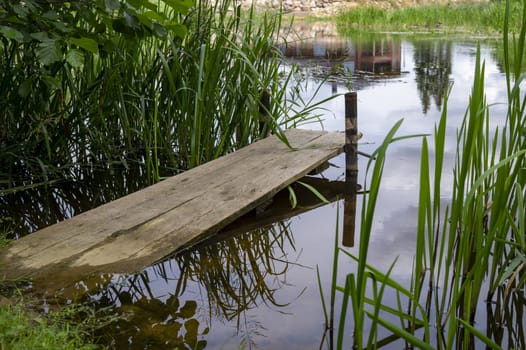 Old rustic wooden jetty on a tranquil lake with reeds and wild grasses on the bank and reflections on the water
