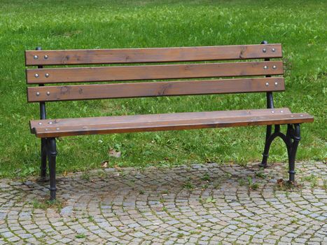 empty wooden iron bench on the park on grass and pavement background