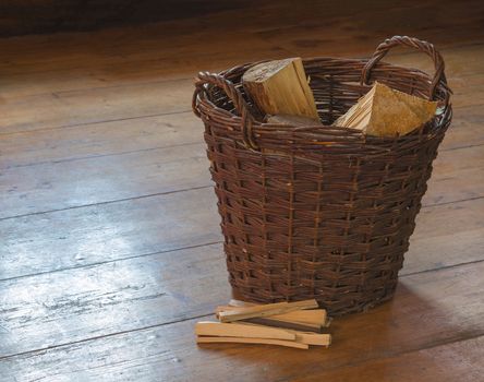 wicker basket with chopped wood and splinter pile on wooden board floor