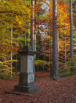 lonely deserted stone memorial monument with cross  in autumn colored orange beech tree forest