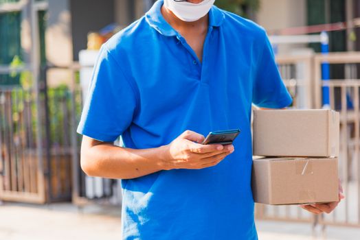 Asian delivery man courier online holding deliveries out boxes and using mobile phone contact the customer he protective face mask service under curfew quarantine pandemic coronavirus COVID-19