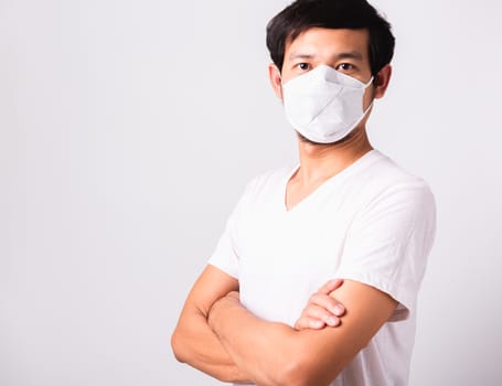 Closeup Asian handsome Man wearing surgical hygienic protective cloth face mask against coronavirus and stand crossed arm, studio shot isolated white background, COVID-19 medical concept