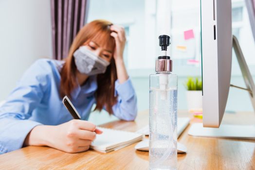 Asian young business woman wearing face mask protective working from home office with laptop computer he quarantines disease coronavirus or COVID-19 and write note booklist work today