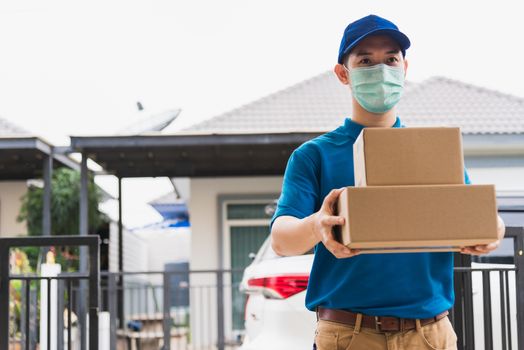 Asian delivery express courier young man giving boxes to woman customer he wearing protective face mask at front home, under curfew quarantine pandemic coronavirus COVID-19