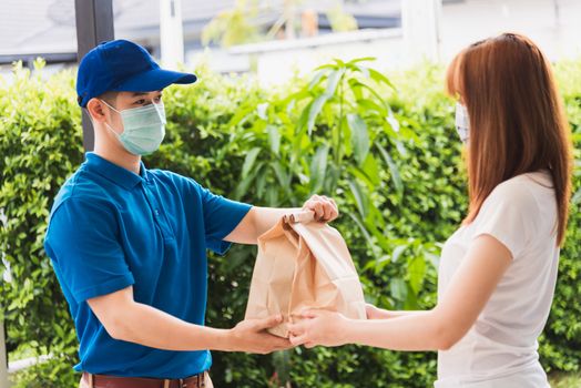 Asian delivery express courier young man giving paper bags fast food to woman customer receiving both protective face mask, under curfew quarantine pandemic coronavirus COVID-19