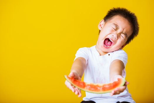 Happy portrait Asian child or kid cute little boy attractive laugh smile playing holds cut watermelon fresh for eating, studio shot isolated on yellow background, healthy food and summer concept