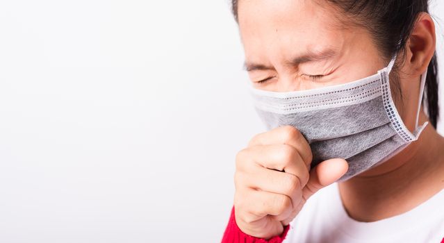 Closeup Asian adult woman wearing red shirt and face mask protective against coronavirus or COVID-19 virus or filter dust, air pollution her sneezing use hand close mouth, isolated white background