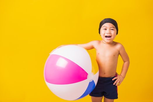 Summer vacation concept, Portrait Asian happy cute little child boy smiling in swimsuit hold beach ball, Kid having fun with inflatable ball in summer vacation, studio shot isolated yellow background