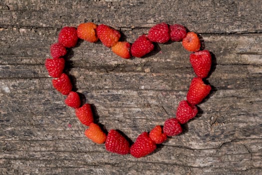 Heart from raspberries on a wooden background.