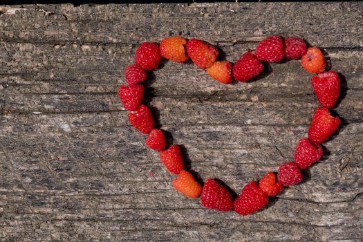 Heart made of ripe aromatic raspberrie on a wooden background.