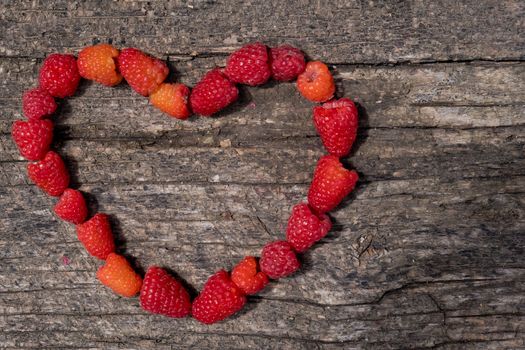 Heart made of ripe aromatic raspberrie on a wooden background.