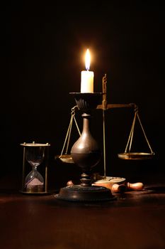Elegant brass candlestick with lighting candle near hourglass and weight scale