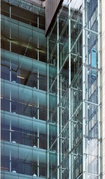 corner view of elevators and stories in a tall modern glass corporate building with walls reflected in the windows