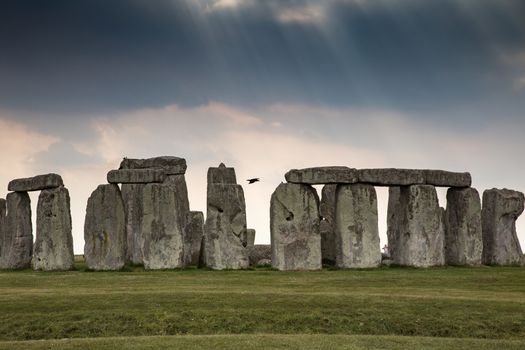 Standing neolithic stones with shafts of heavenly sunlight through dark threatening clouds