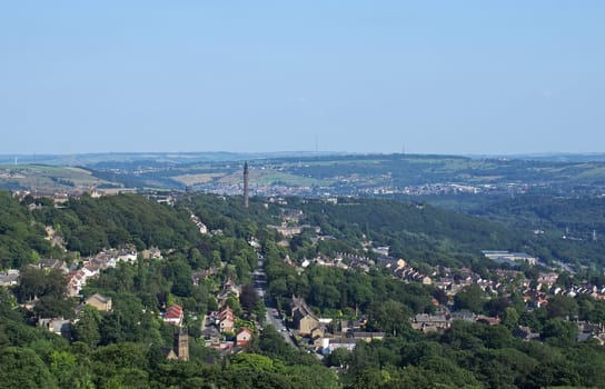 a panoramic view of the town of west yorkshire from above with streets and houses surrounded by trees and fields and the historic wainhouse tower on a hillside
