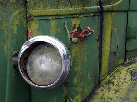 close up of the headlight of an old abandoned truck with rusted green grille and panels