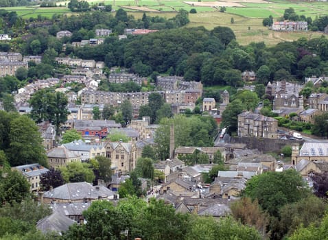 an aerial view of the town of hebden bridge with streets and houses surrounded by summer trees and fields