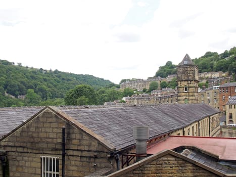 a view of the steep hillside streets in hebden bridge between summer trees with the tower of the historic nutclough mill building at the front