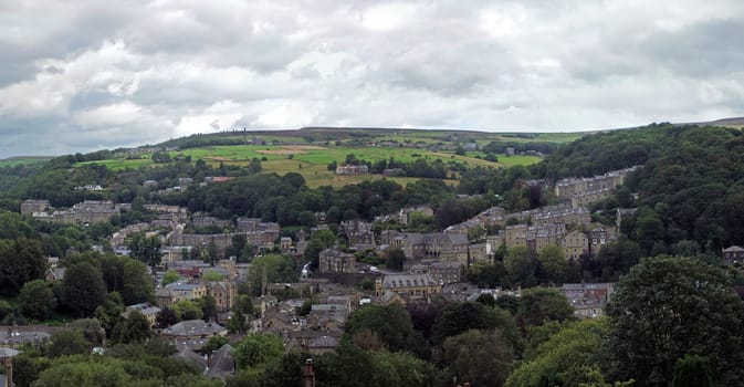 a wide panoramic view of the town of hebden bridge with hillside streets surrounded by trees and pennine fields