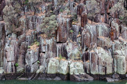 Rock face at Cataract Gorge in Launceston, Tasmania Australia. Delicate colours of rocks with trees and textures down to waters edge High quality photo