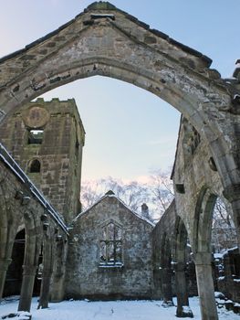 the medieval ruined church in heptonstall covered in snow showing arches and columns against a blue winter sky