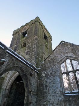 the medieval ruined church in heptonstall covered in snow showing arches and tower and windows against a blue winter sky